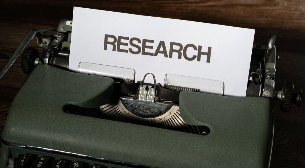 Obrazek przedstawia maszynę do pisania, w której włożona jest biała kartka papieru. Na kartce jest napis "research".